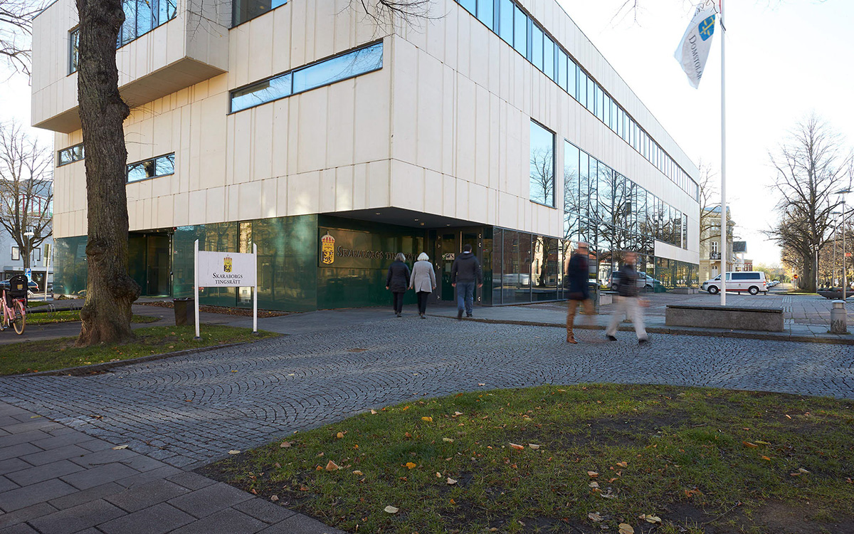 Bilden visar en stor vit och massiv byggnad. Några personer ses gå framför den. Men man ser inte deras ansikten, bilden är tagen på avstånd och fokus ligger på byggnaden.