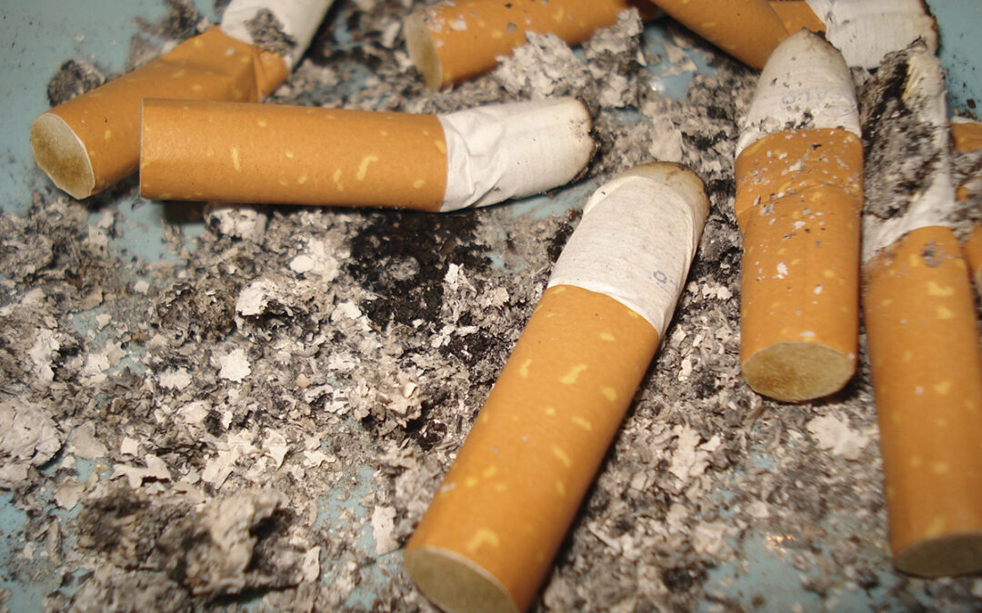 Några fimpade cigaretter och aska i närbild mot turkosgrå bakgrund (ett askfat?). Uppsalahem kräver en tidigare hyresgäst på en stor summa pengar, bland annat för sanering av lägenheten efter att någon eller några rökt inomhus.