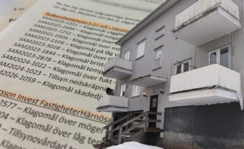 Ett gråmålat slitet trähus monterat med en bakgrund av papper med klagomålslista.