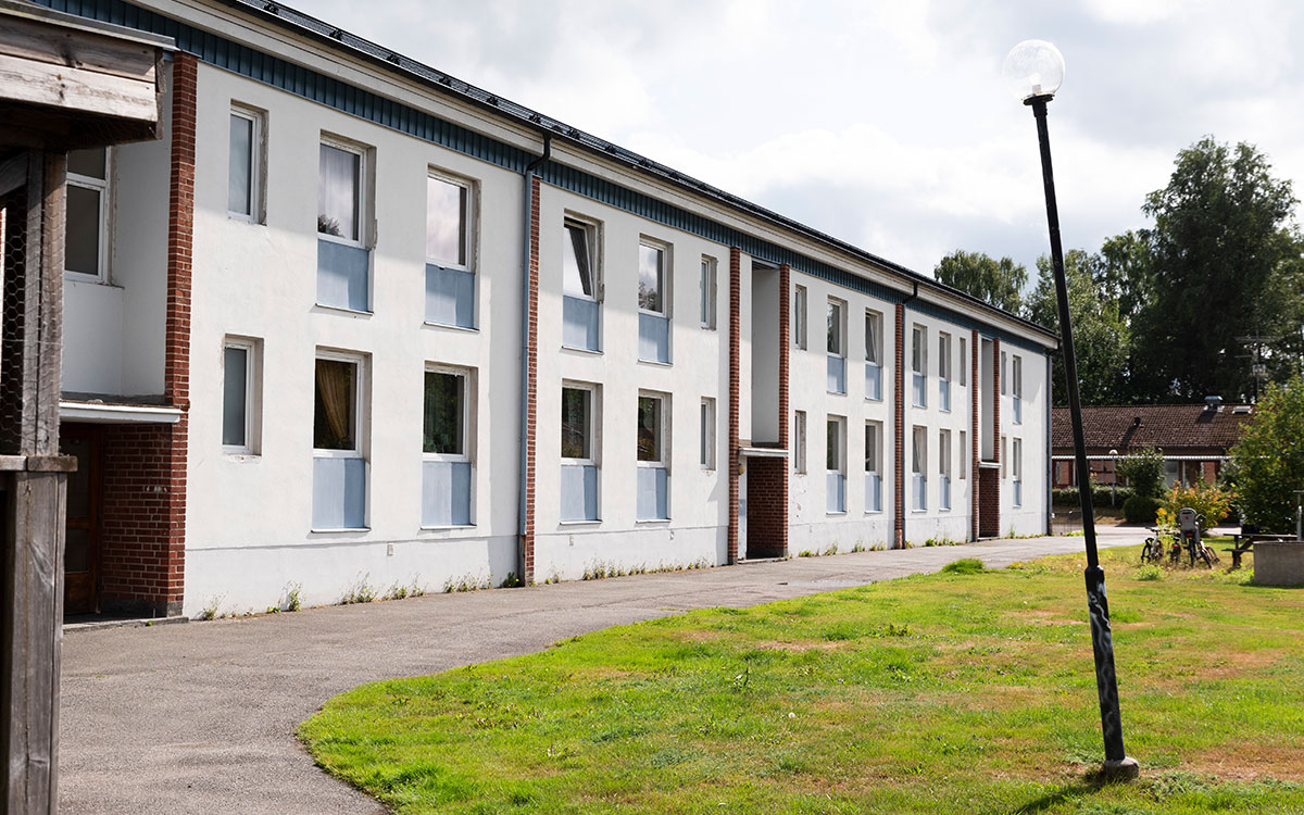 Ett flerfamiljshus i två våningar och en sned lyktstolpe på en gräsmatta.