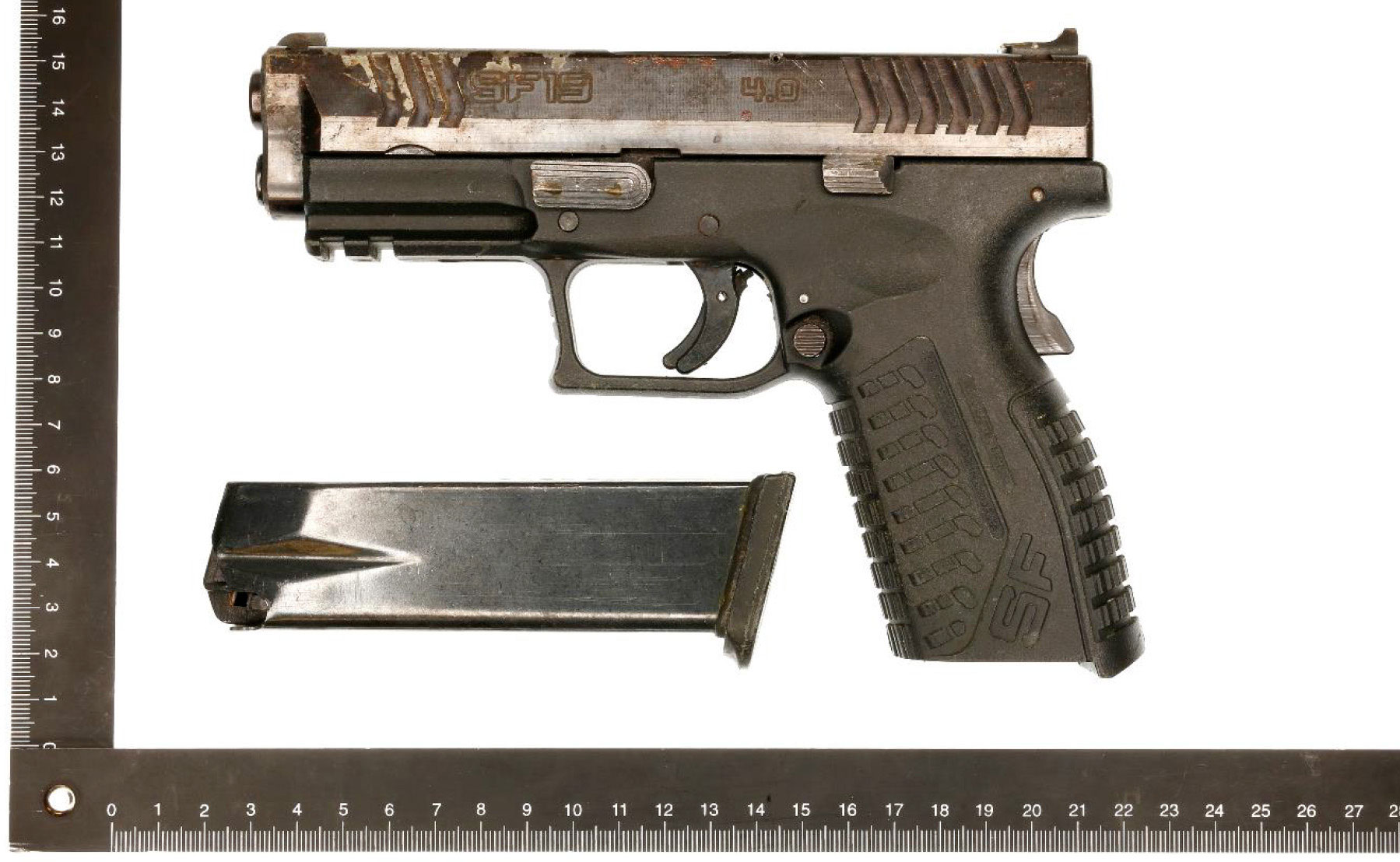 En bild som visar en pistol samt tillhörande magasin fotograferad bredvid en linjal för måttangivelser.