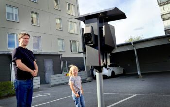 En man och ett barn står framför ett hus och intill en laddstolpe.