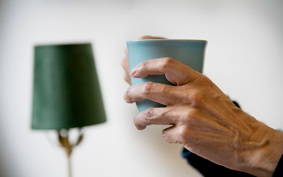 Annas hand håller i en mugg, en lampskärm i bakgrunden