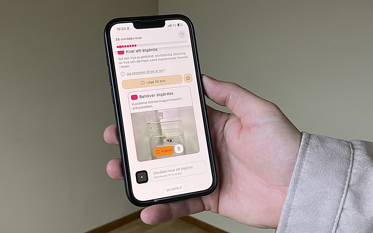 En hand håller i en mobiltelefon som visar AI-appen som ska hjälpa till vid flyttstädning. "Behöver åtgärdas" står det vid fotot på insidan av ett kylskåp där det ligger något på en hylla.