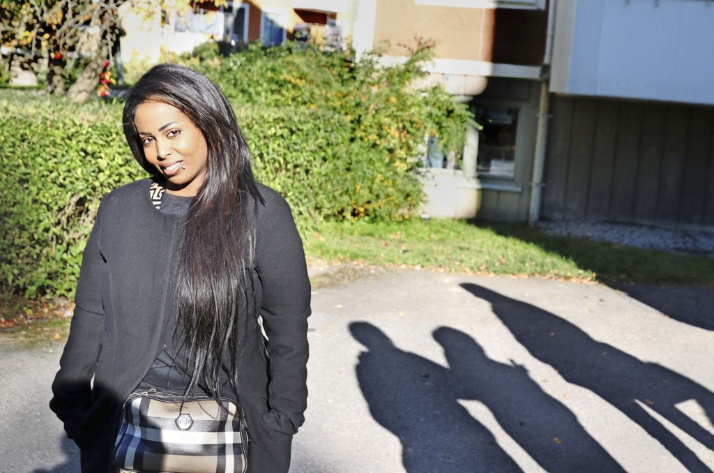 2108MIT_återbruk2 Kvinna står utanför ett hus och intill personer som syns som skuggor.