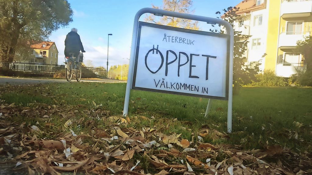 En skylt som står ute i höstlöven som berättar att återbruket har öppet.