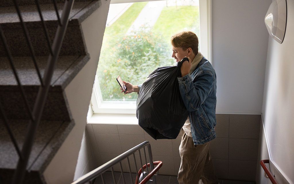 Albin bär en stor soppåse nedför trapporna och spelar in en video samtidigt.