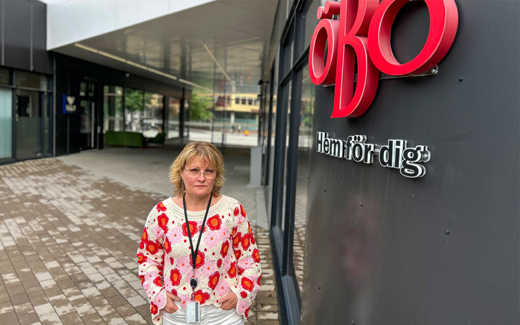 Kvinna i röd och vit blus som står längs en vägg där delar av Öbo-loggan syns
