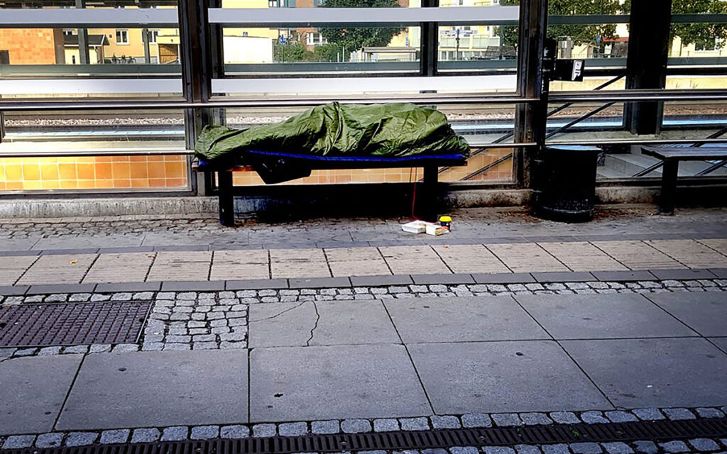 Hemlös busskur En person ligger på en parkbänk insvept i grön presenning.