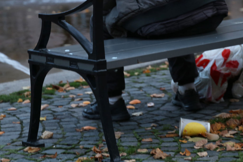 En kraftigt beskuren bild där bara benen syns på en man som sitter på en parkbänk.