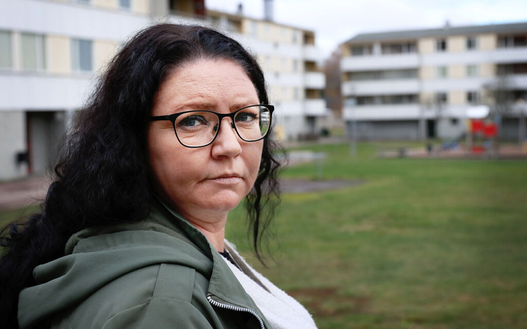 Caroline En kvinna i grön jacka och mörkt hår står framför några vita flerfamiljshus.