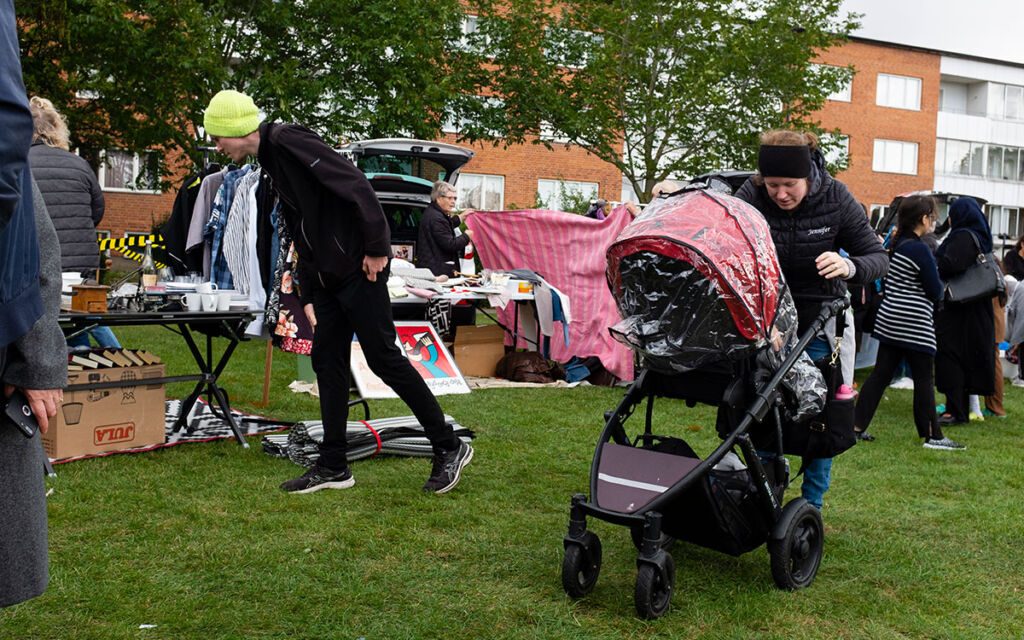 En man som böjer sin ned för att titta på ett bord på en loppmarknad och en kvinna som tittar in i den barnvagn hon kör.