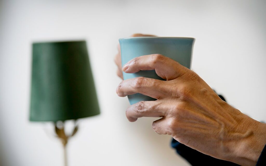 Annas hand håller i en mugg, en lampskärm i bakgrunden