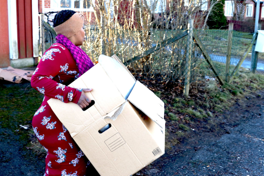 En kvinna i röd klänning bär en flyttkartong utomhus.